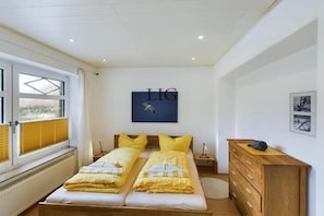 Een slaapkamer met twee bedden, een houten dressoir, een radiator en een raam met zonwering.