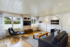 A modern living room with a sofa, armchair, coffee table, and a TV mounted on the wall. - Holiday apartment Palladium 1 (Langeoog)