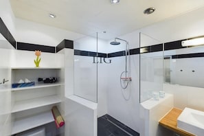 Een moderne badkamer met een douche in een glazen cabine, witte tegels en een houten wastafelmeubel.