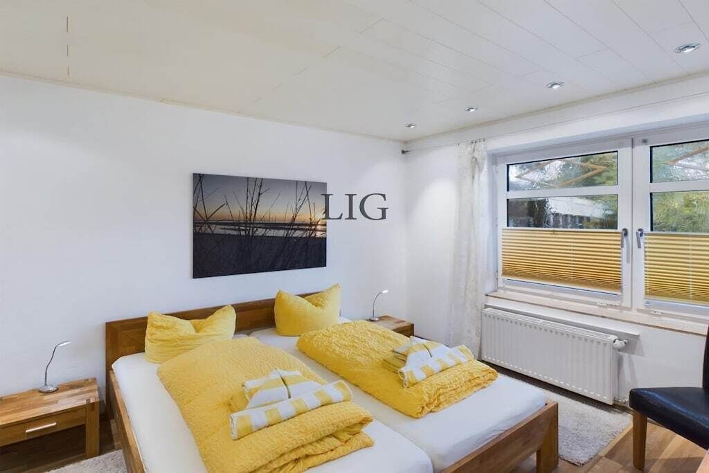 A bedroom with two beds, a window with blinds, a radiator, and a wall-mounted artwork.