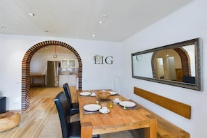 Een eethoek met een houten tafel voor vier personen, een spiegel aan de muur, en een keuken op de achtergrond.