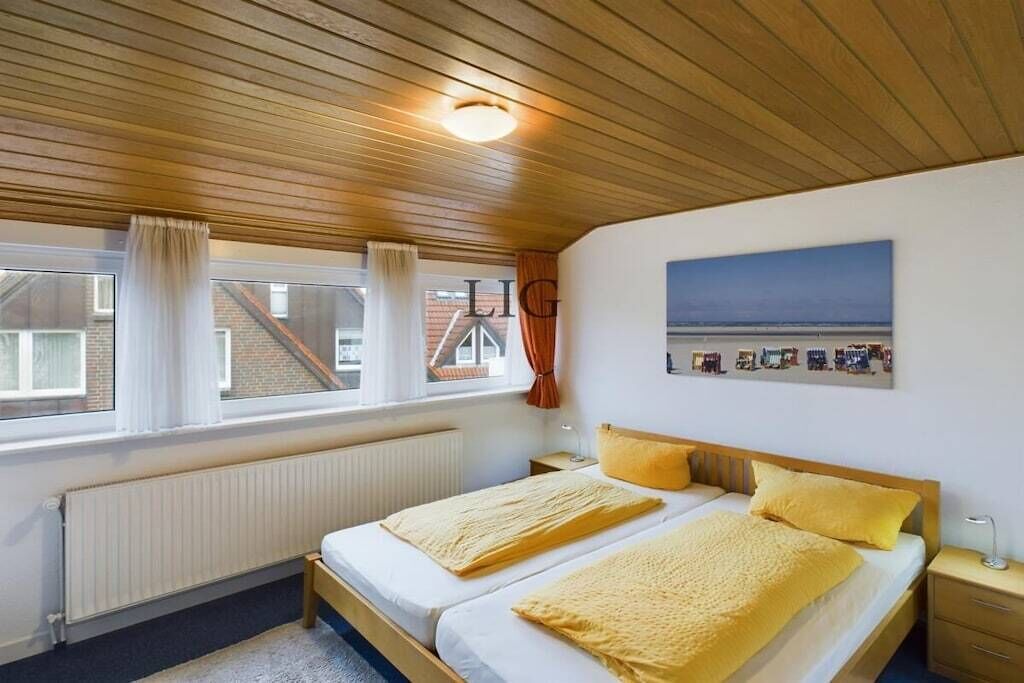 A bedroom with two beds, a view of the sea through the window, and a painting on the wall.
