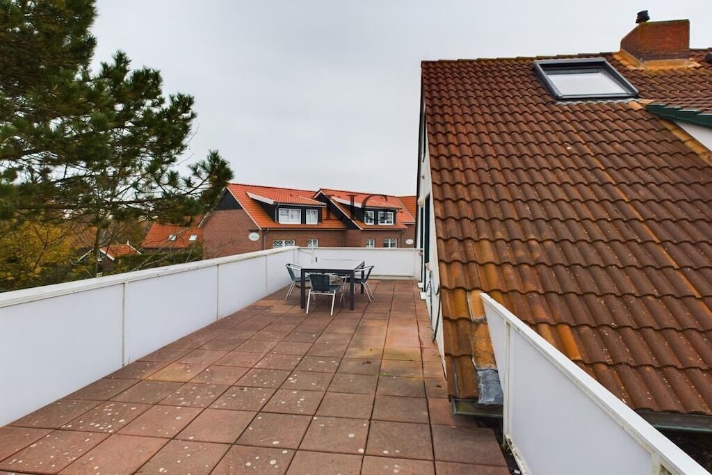 Une terrasse sur le toit, avec une table et des chaises, un toit recouvert de tuiles et un bâtiment voisin doté d’un toit en pente.