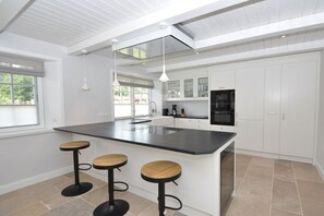 A modern kitchen with a central island, bar stools, and white cabinetry. - Holiday home with 4 bedrooms (Sankt Peter Ording)