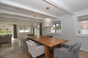 Un comedor amplio con una mesa de madera y sillas tapizadas en gris, ventanas grandes y un techo alto con vigas a la vista.