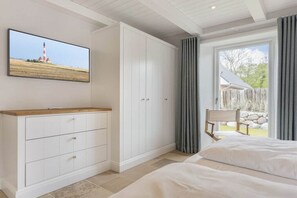 Une chambre à coucher comprenant un lit, une armoire, un téléviseur fixé au mur et une vue sur l’extérieur par une fenêtre.