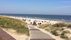 A beach pathway leading to beach chairs and umbrellas, with the ocean in the background. - Holiday apartment Lighthouse view (Wangerooge)