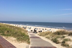 Un sentiero sulla spiaggia conduce a sedie a sdraio e ombrelloni, con l'oceano sullo sfondo.