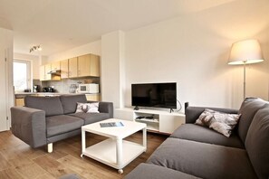 A modern living room with a grey sofa, a white coffee table, a flat-screen TV, and a lamp. - Holiday apartment Lighthouse view (Wangerooge)