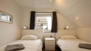 A bedroom with two beds, a nightstand, a window with curtains, and a radiator. - Holiday apartment Lighthouse view (Wangerooge)