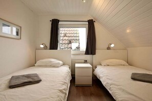Camera da letto con due letti, un comodino, una finestra con tende e un termosifone.