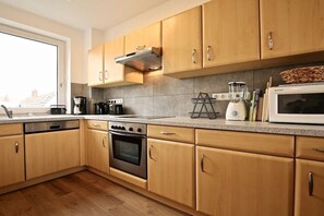 A modern kitchen with wooden cabinets, a built-in oven, a coffee maker, and a microwave. - Holiday apartment Lighthouse view (Wangerooge)