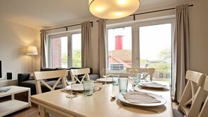 A dining area with a table set for four, a sofa, and a lamp. - Holiday apartment Lighthouse view (Wangerooge)