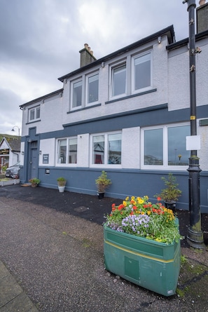 A two-story building with a flat roof and a large window on the ground floor. - Cosy former converted bank in heart of a busy working fishing village. (Mallaig)