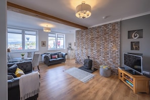 A living room with a brick wall, a fireplace, a sofa, a TV, and a view of the outside.