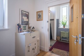 A hotel room with a wooden cabinet, a framed picture, a window with a view, and a door with a key lock.