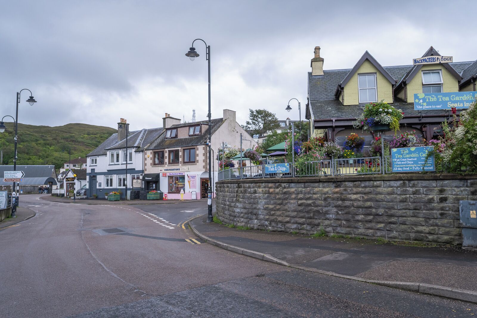 A street view with a row of buildings, including a cafe named 'The Tea Garden Cafe' and a sign for 'Backpackers Lodge'.
