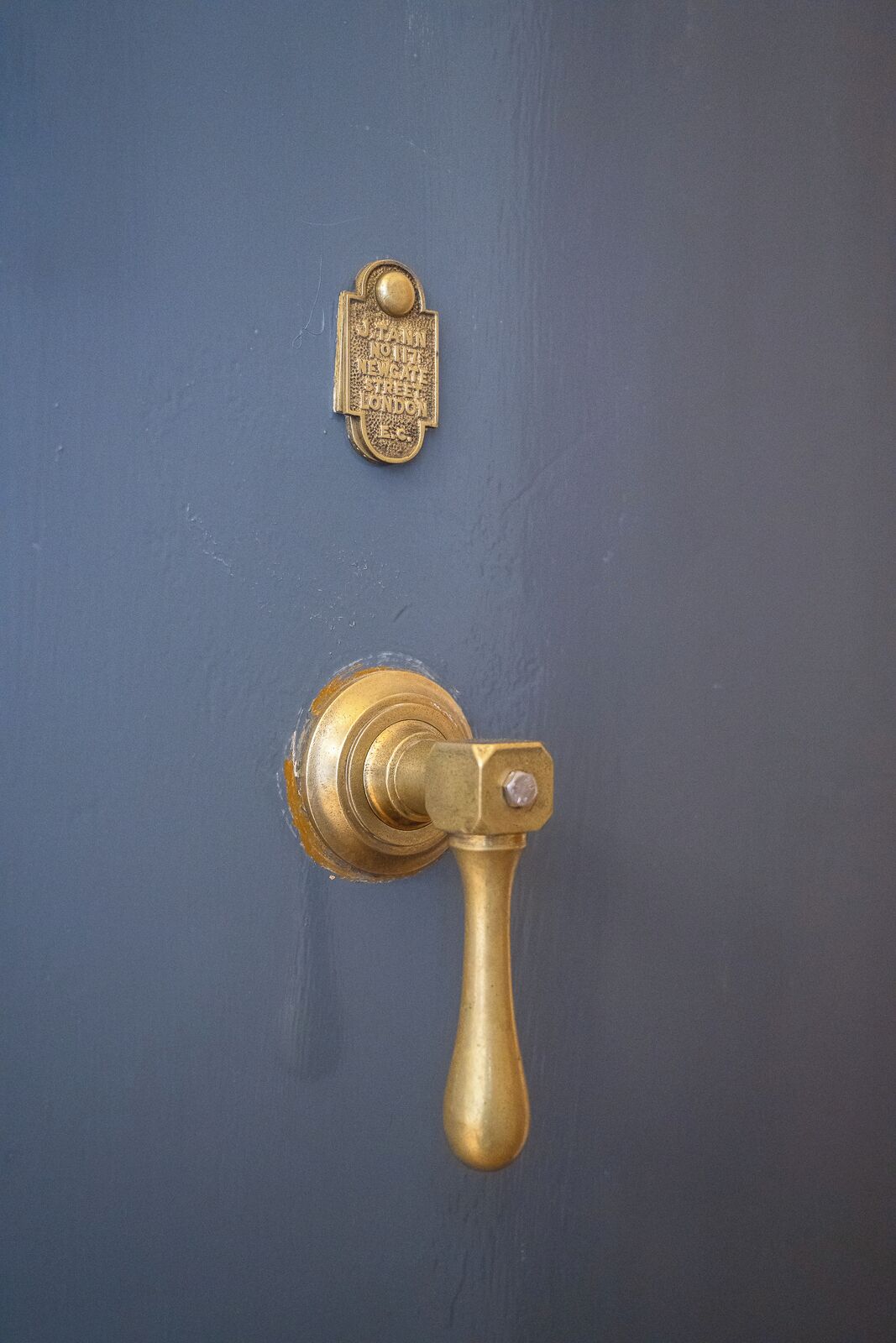 Une poignée de porte en laiton et une plaque en laiton portant l’inscription « NEW GATE THE LONDON » sur une porte bleue.