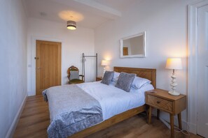 A bedroom with a wooden bed, bedside lamps, a chair, and a mirror on the wall. - Cosy former converted bank in heart of a busy working fishing village. (Mallaig)