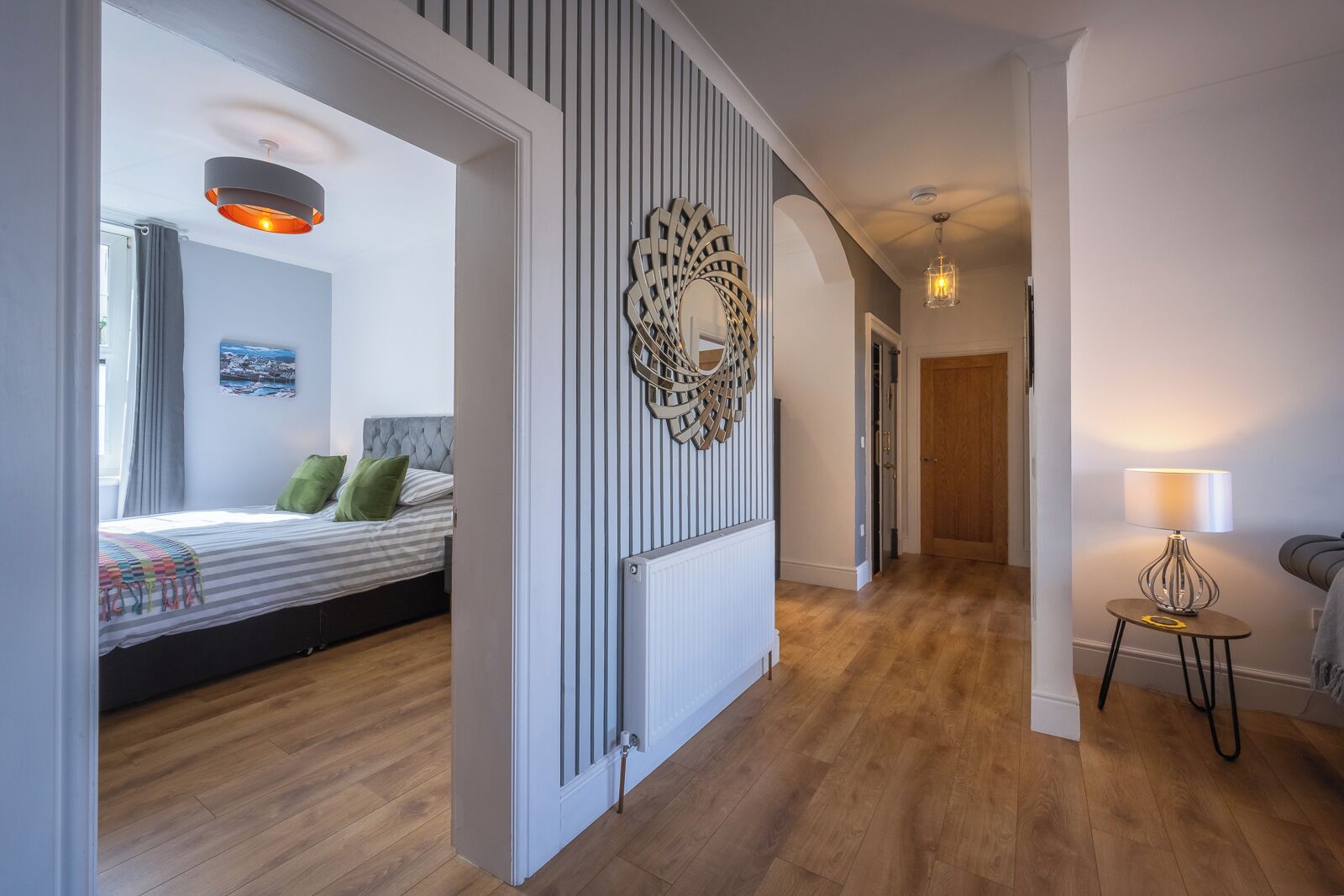 A modern bedroom with a bed, a decorative wall piece, and a hallway leading to another room.