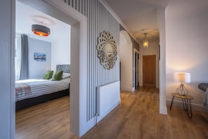 A modern bedroom with a bed, a decorative wall piece, and a hallway leading to another room. - Cosy former converted bank in heart of a busy working fishing village. (Mallaig)