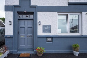 A building facade with a dark blue door, a sign for Maoldon Bank, and two potted plants.