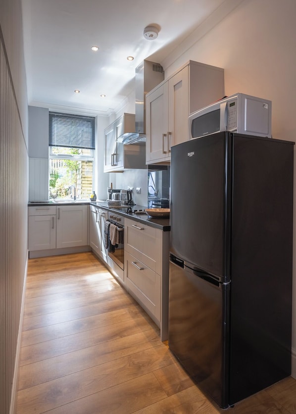 A modern kitchen with a black refrigerator, stainless steel appliances, and wooden flooring.