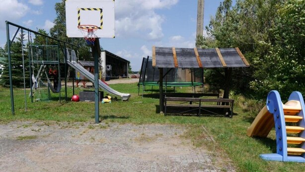 Une aire de jeux avec un panier de basket, un toboggan et une balançoire.