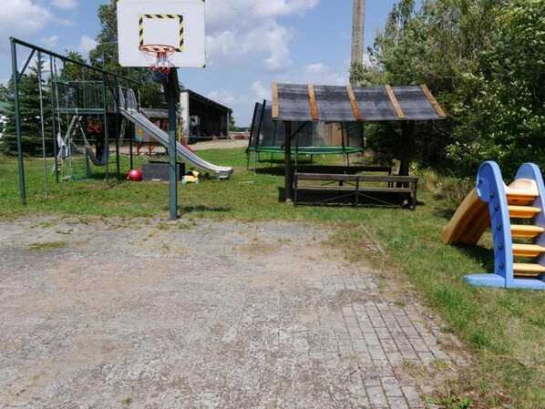 A playground with a basketball hoop, a slide, and a swing set.