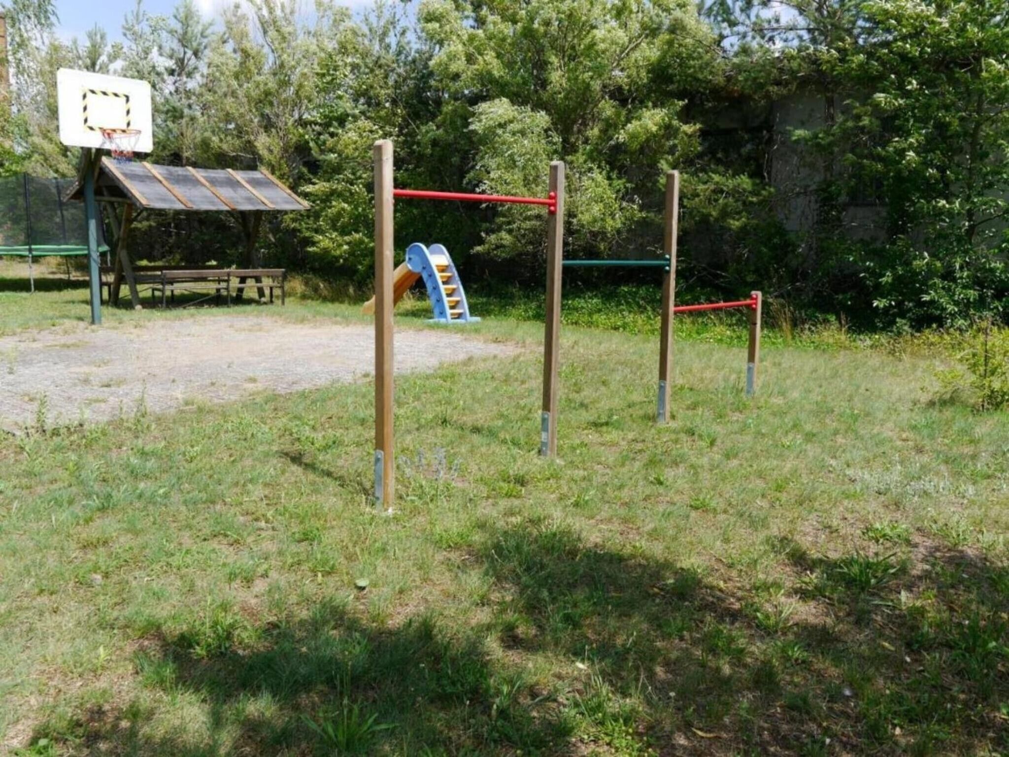 Ein Spielplatz im Freien mit Basketballkorb, Rutsche und Klettergerüst.