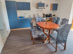 A compact kitchen with blue cabinets, a wooden dining table, and matching chairs. - Spacious Apartment with Private Garden and Wi-Fi in Milmersdorf (Milmersdorf)