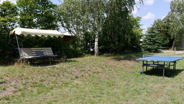 Un espace extérieur comprenant une table de ping-pong, un coin salon abrité et une balançoire.