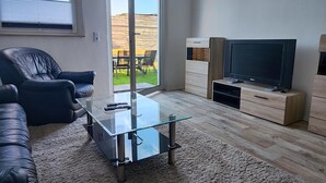 Un salon moderne avec une table basse en verre, un canapé en cuir et un téléviseur à écran plat posé sur un meuble en bois.