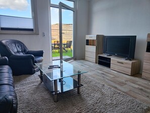 A modern living room with a glass coffee table, leather sofa, and a flat-screen TV on a wooden stand.