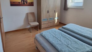 Une chambre avec une armoire en bois, une chaise, un lit avec une literie à motifs et un tableau représentant un éléphant.
