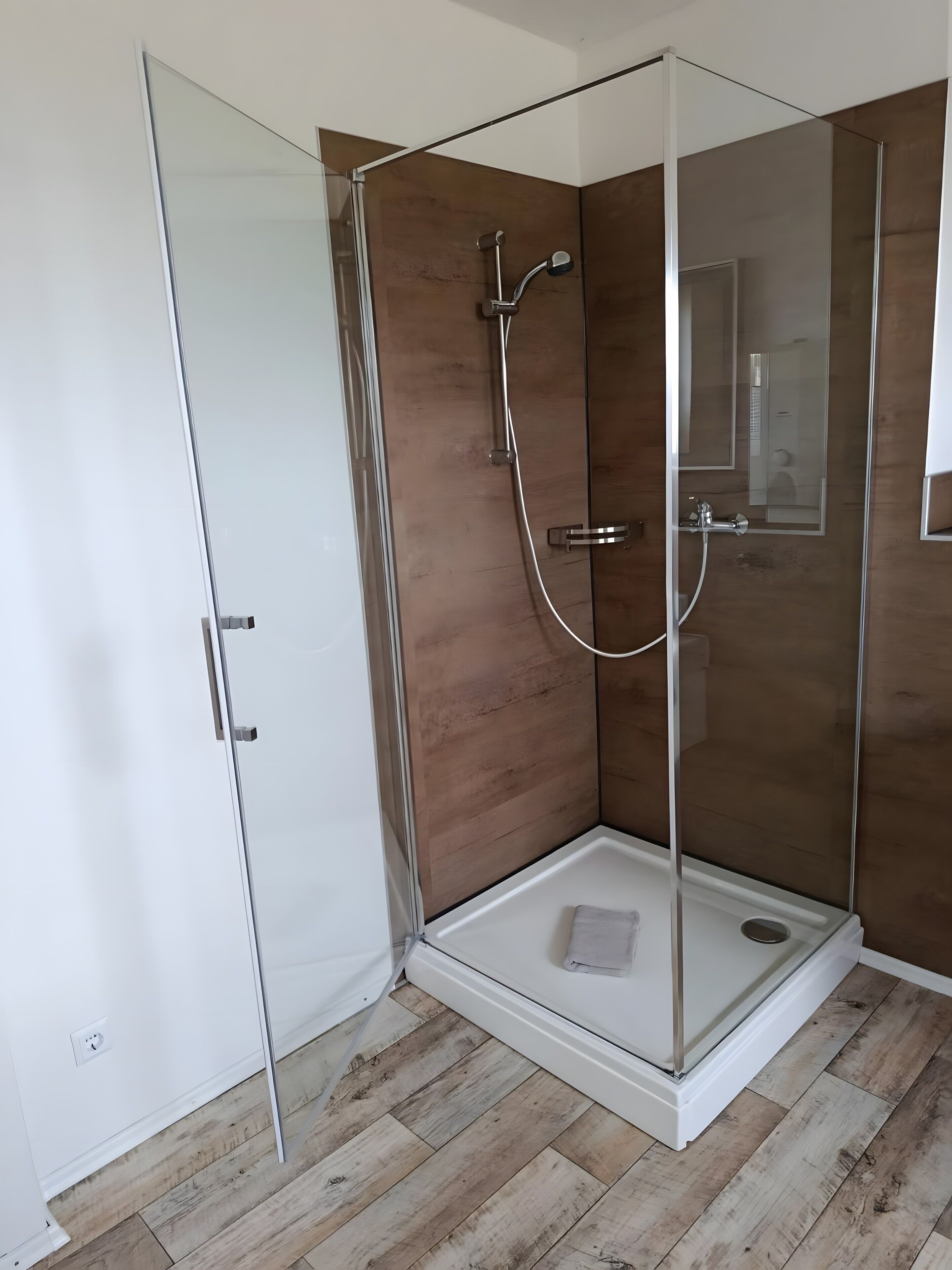 Une douche entièrementClose avec des parois en verre, un mur en bois et un sol blanc.