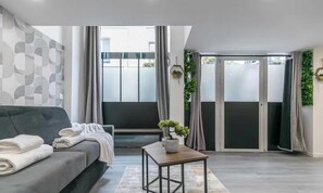 A modern living room with a sofa, a small table, and a sliding glass door leading to a balcony. - Apartment Cosy - 2BR/6P - Near Montorgueil (Paris)