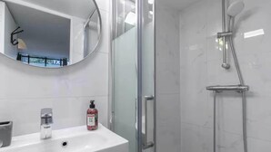A modern bathroom with a glass shower enclosure, a white sink, and a mirror. - Apartment Cosy - 2BR/6P - Near Montorgueil (Paris)