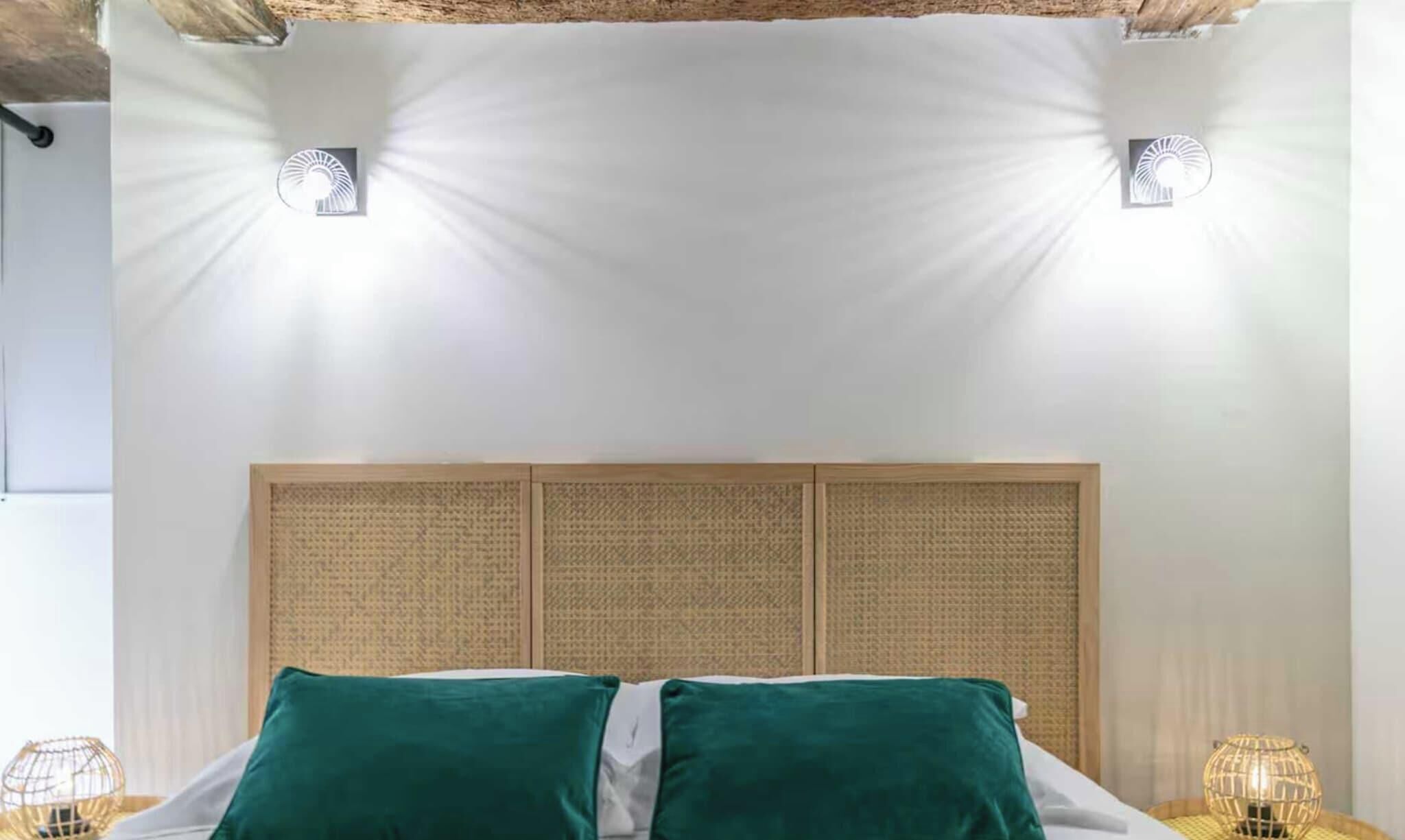A bed with green pillows, a woven headboard, and two wall-mounted lights.