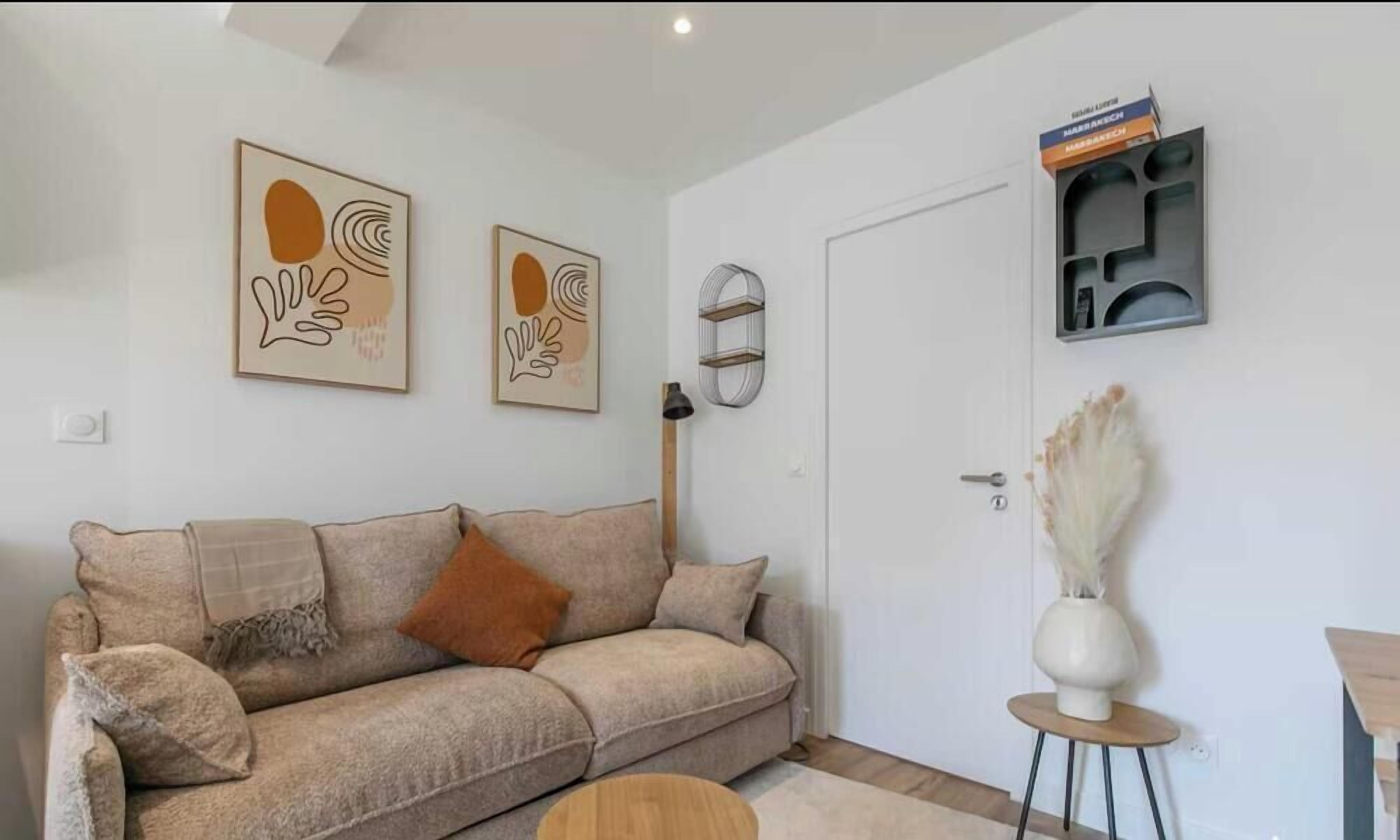 Un soggiorno con un divano color beige, due opere d'arte astratte incorniciate, una porta e un tavolino con un vaso.