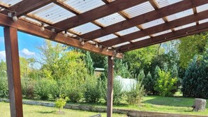 An outdoor patio with a wooden pergola, a table with chairs, and a brick floor.