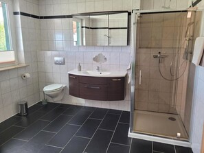 A bathroom with a toilet, a sink with a mirror, and a shower enclosure. - Apartment with Garden, Terrace, Private Garden & Wi-Fi in Milmersdorf (Milmersdorf)