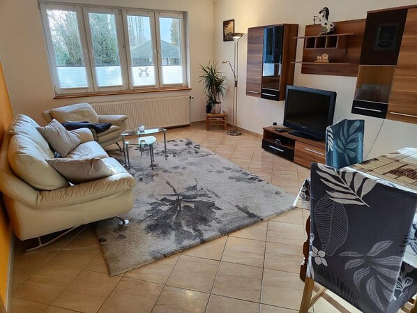 A living room with a sofa, a coffee table, a TV, and a plant. - Apartment with Garden, Terrace, Private Garden & Wi-Fi in Milmersdorf (Milmersdorf)