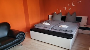 A bedroom with a bed, a black leather chair, and a nightstand with a lamp.