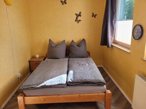 A bed with a wooden frame, two pillows, and a blanket in a room with yellow walls. - Apartment with Garden, Terrace, Private Garden & Wi-Fi in Milmersdorf (Milmersdorf)