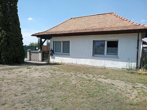 A single-story house with a tiled roof, two windows, and a fenced yard. - Holiday Home with Terrace, Wi-Fi & Parking in Uckermark for 2–3 Guests (Milmersdorf)