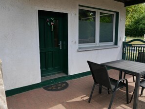 A patio with a table and chairs, a green door, and a window. - Holiday Home with Terrace, Wi-Fi & Parking in Uckermark for 2–3 Guests (Milmersdorf)
