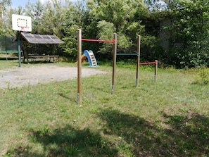 An outdoor playground with a basketball hoop, a slide, and a climbing structure.