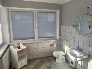 A bathroom with a toilet, sink, and window with blinds. - Holiday Home with Terrace, Wi-Fi & Parking in Uckermark for 2–3 Guests (Milmersdorf)