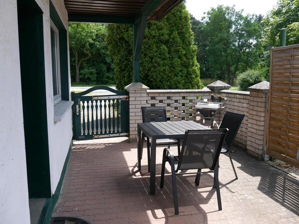 An outdoor patio with a table and chairs, a brick wall, and a green gate. - Holiday Home with Terrace, Wi-Fi & Parking in Uckermark for 2–3 Guests (Milmersdorf)
